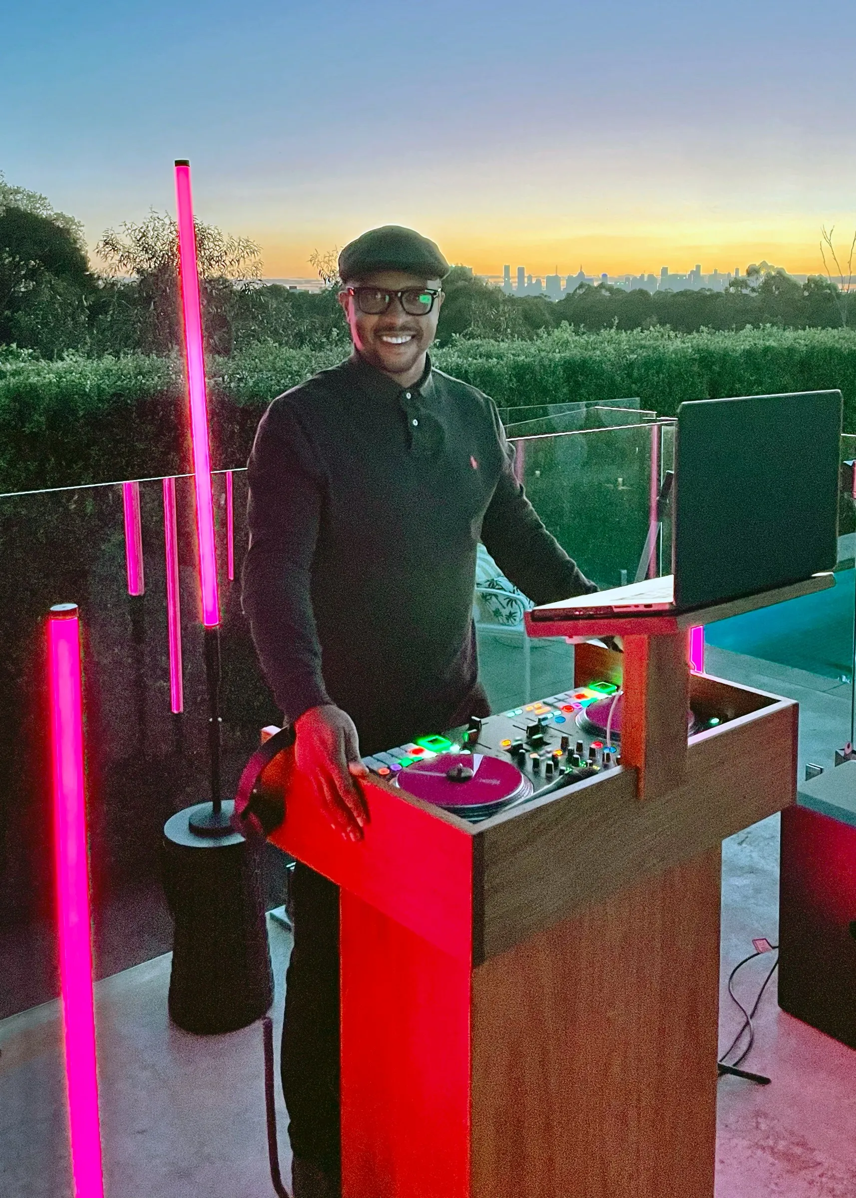 Dan at his booth on a terrace at sunset, magenta tube lights glowing either side