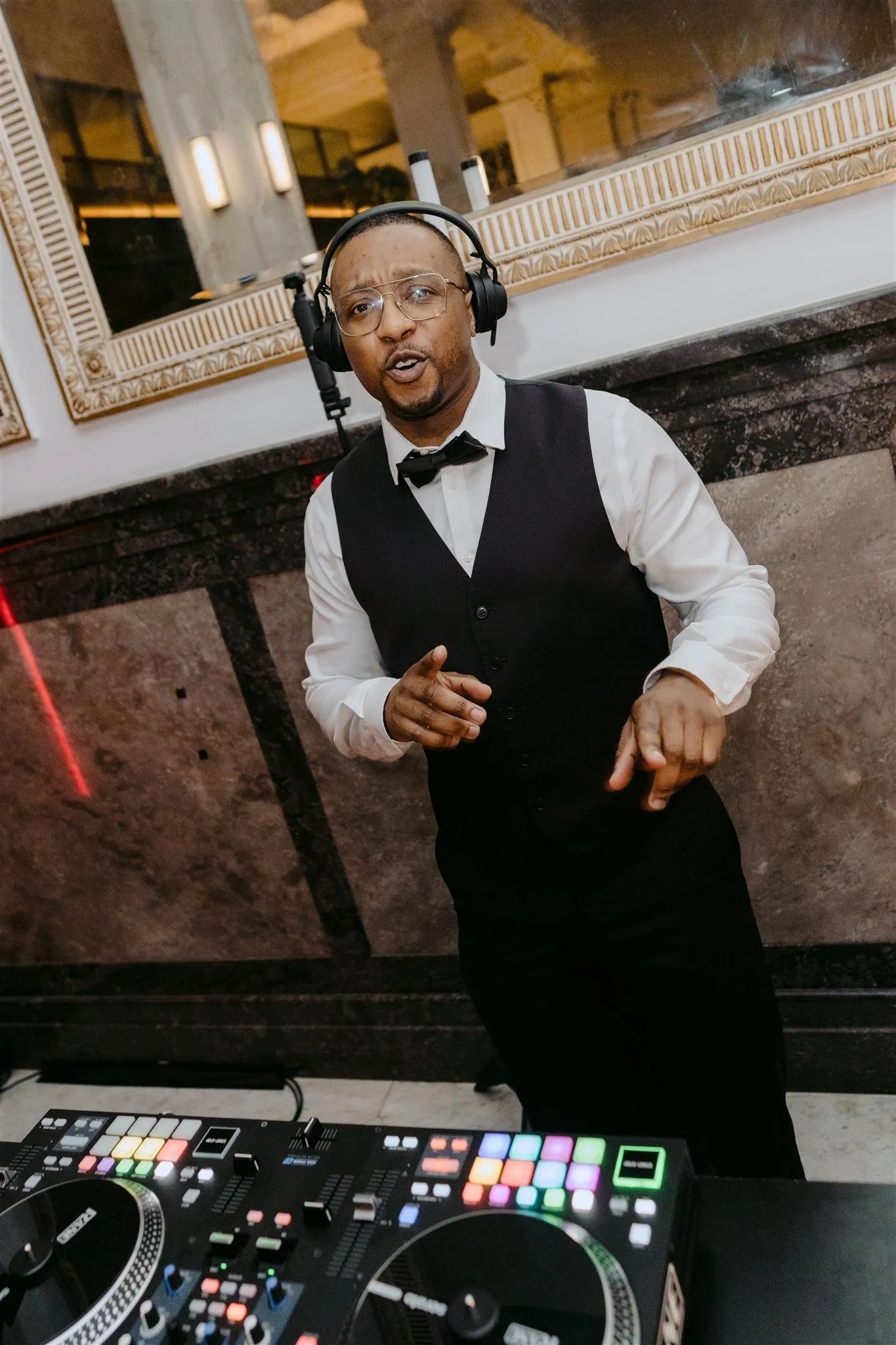 Dan in a bow tie and headphones behind the decks at a wedding reception, mid-mix