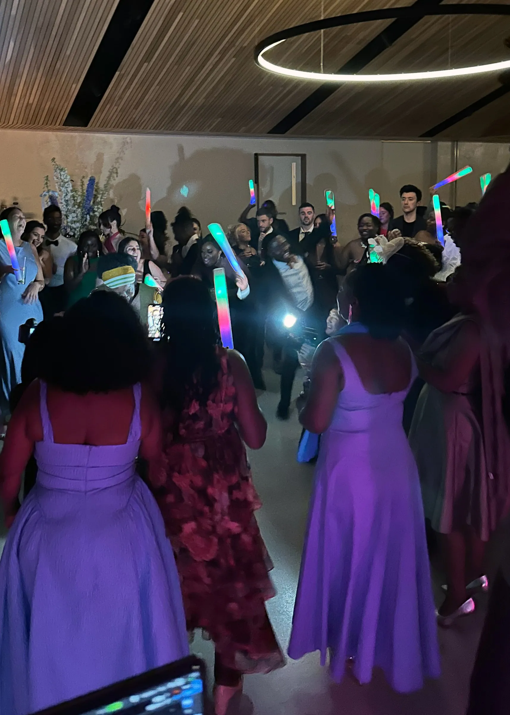 Bridesmaids in lilac dancing with glow sticks on a crowded wedding dance floor